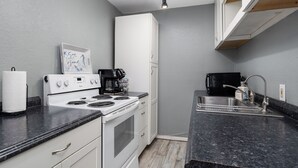A compact kitchen with a stove, sink, and white cabinets.