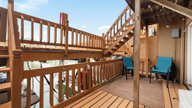A wooden deck with a railing, a staircase, and a seating area with chairs.
