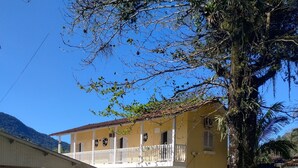 A yellow building with a balcony and a tree in front. - NOVO ENCANTO (Ubatuba)