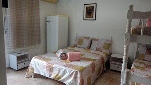A bedroom with a bed, a wardrobe, a bedside table, a nightstand, a window with curtains, and a wall-mounted air conditioner. - NOVO ENCANTO (Ubatuba)