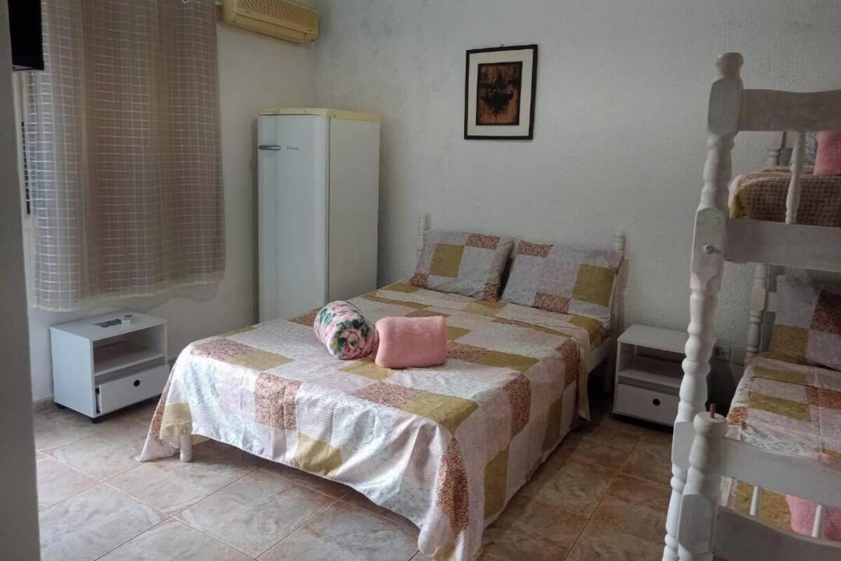 A bedroom with a bed, a wardrobe, a bedside table, a nightstand, a window with curtains, and a wall-mounted air conditioner.