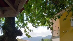 A building with a covered outdoor area, a large tree, and a view of mountains in the background. - NOVO ENCANTO (Ubatuba)