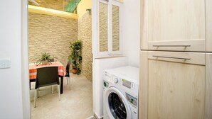 A compact laundry room with a washing machine, a table with chairs, and a potted plant.