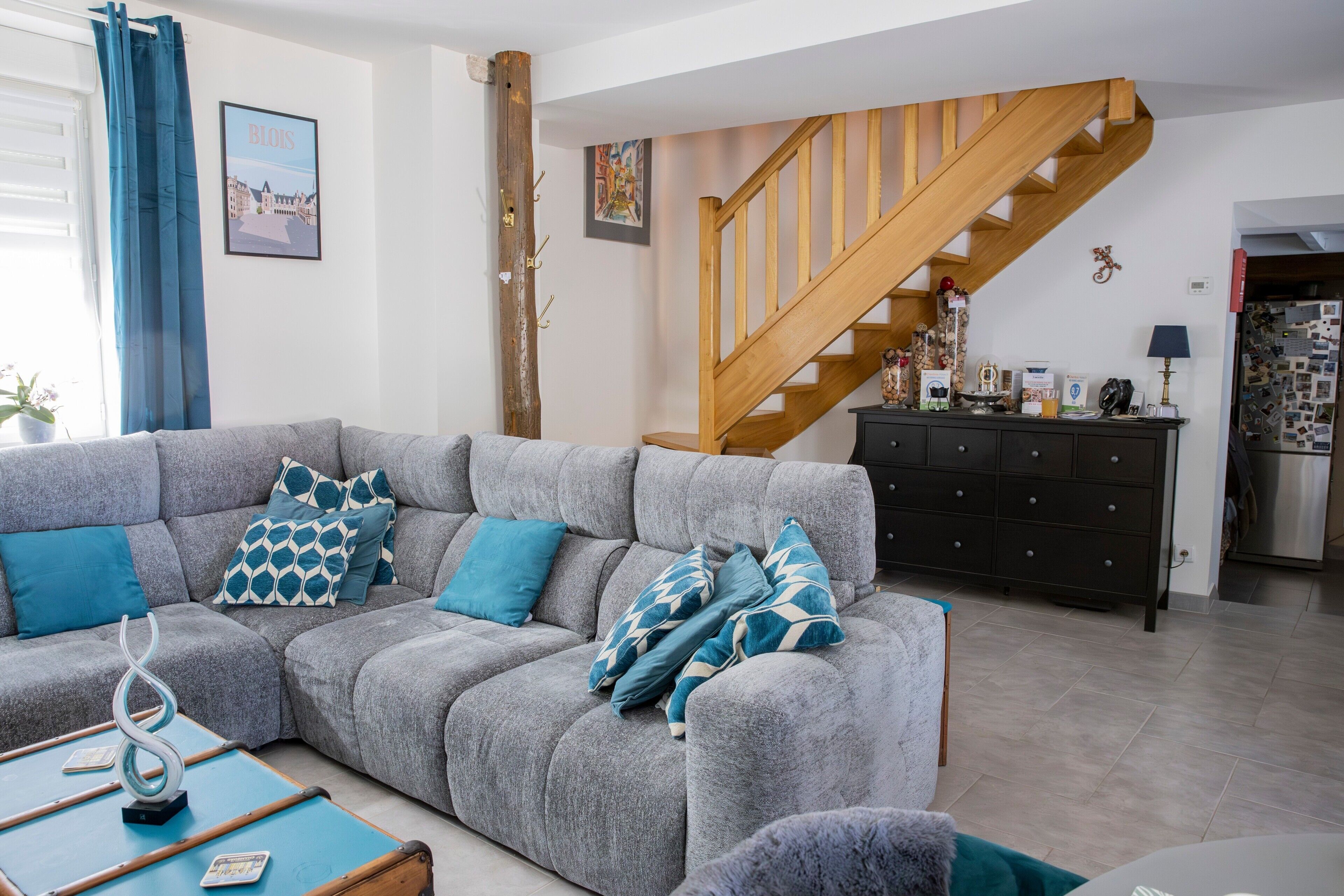 A living room with a grey sectional sofa, a wooden staircase, and a dark wooden cabinet.