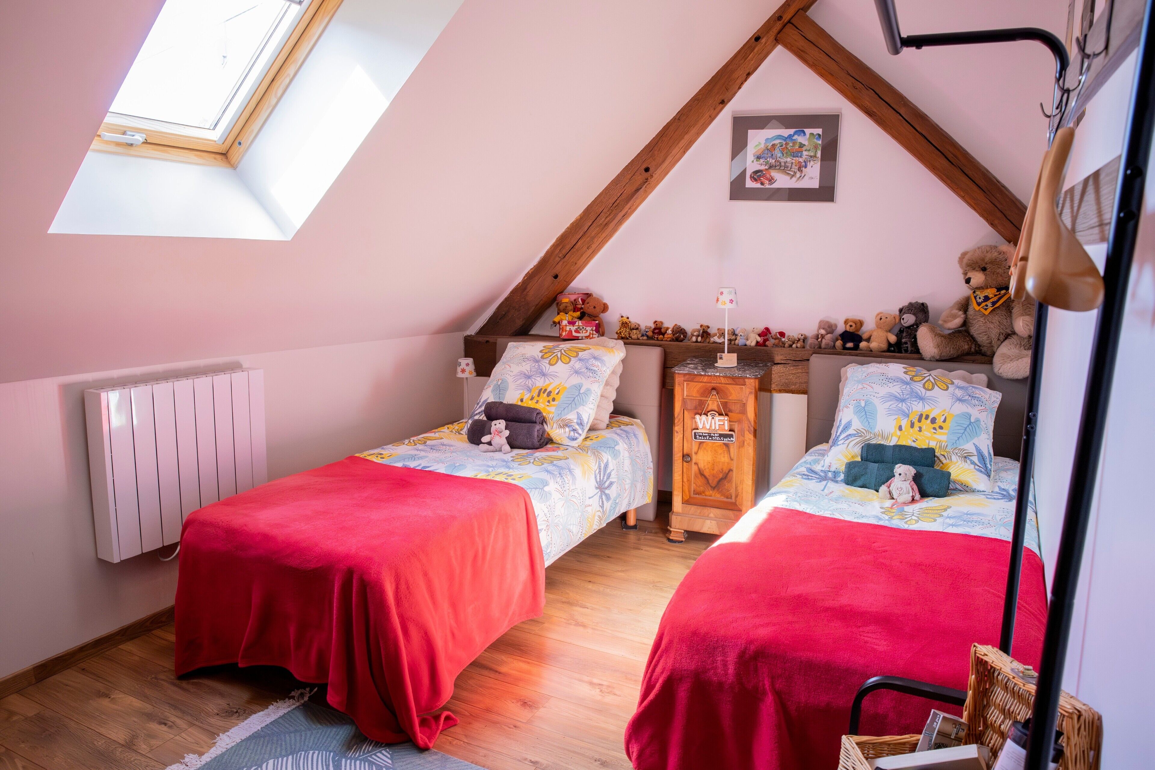 A bedroom with two beds, a skylight, a radiator, a wooden cabinet, and a teddy bear.
