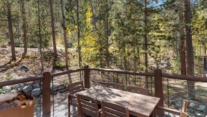 Une terrasse en bois avec une table et des chaises donnant sur une zone boisée.