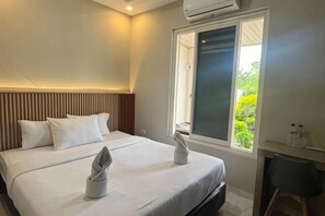 A hotel room with a bed, a desk, and a window with a view of greenery.