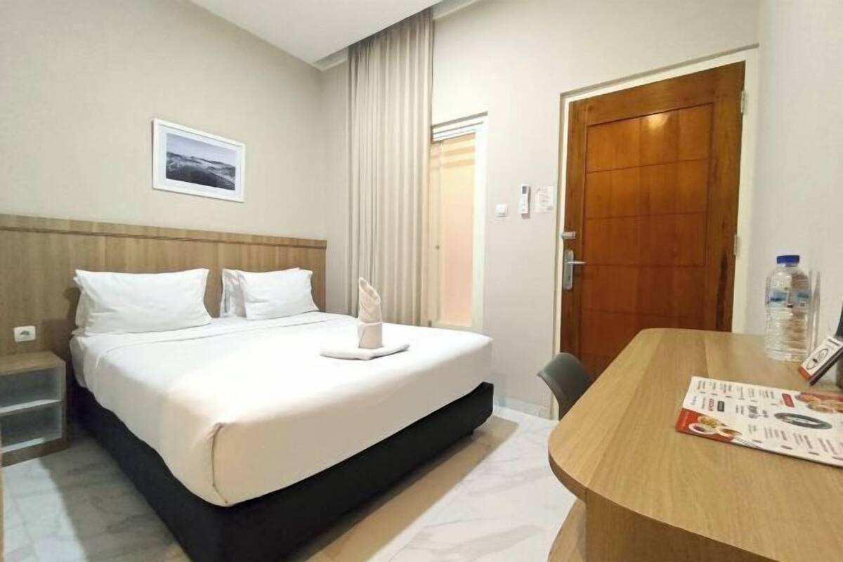 Ein Hotelzimmer mit Bett, einer Holztür, einem kleinen Tisch mit Karte und einem Bild an der Wand.