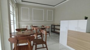 Un espace repas avec des chaises en bois et une table ronde, un comptoir d’accueil blanc et un sol en marbre.