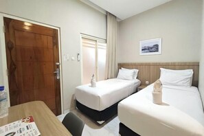 Een hotelkamer met twee bedden, een houten deur, een raam met gordijnen en een lijst met een afbeelding aan de muur.
