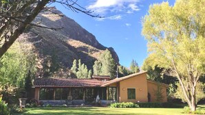 A building with a tiled roof, surrounded by a well-maintained lawn and trees, with a mountain in the background. - w Peaceful 4BR Villa With Nature View (Pisac)