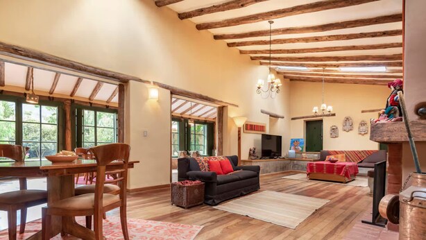 A spacious living room with a wooden ceiling, a fireplace, a sofa, and a dining area with chairs and a table. - w Peaceful 4BR Villa With Nature View (Pisac)