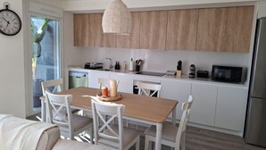 A modern kitchen with wooden cabinets, a dining table with chairs, a hanging light fixture, and a clock on the wall. - Residencial Breeze 1A by Bookaparadise (Finestrat)