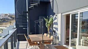A modern outdoor patio with a wooden table and chairs, a potted plant, and a view of the surrounding area. - Residencial Breeze 1A by Bookaparadise (Finestrat)