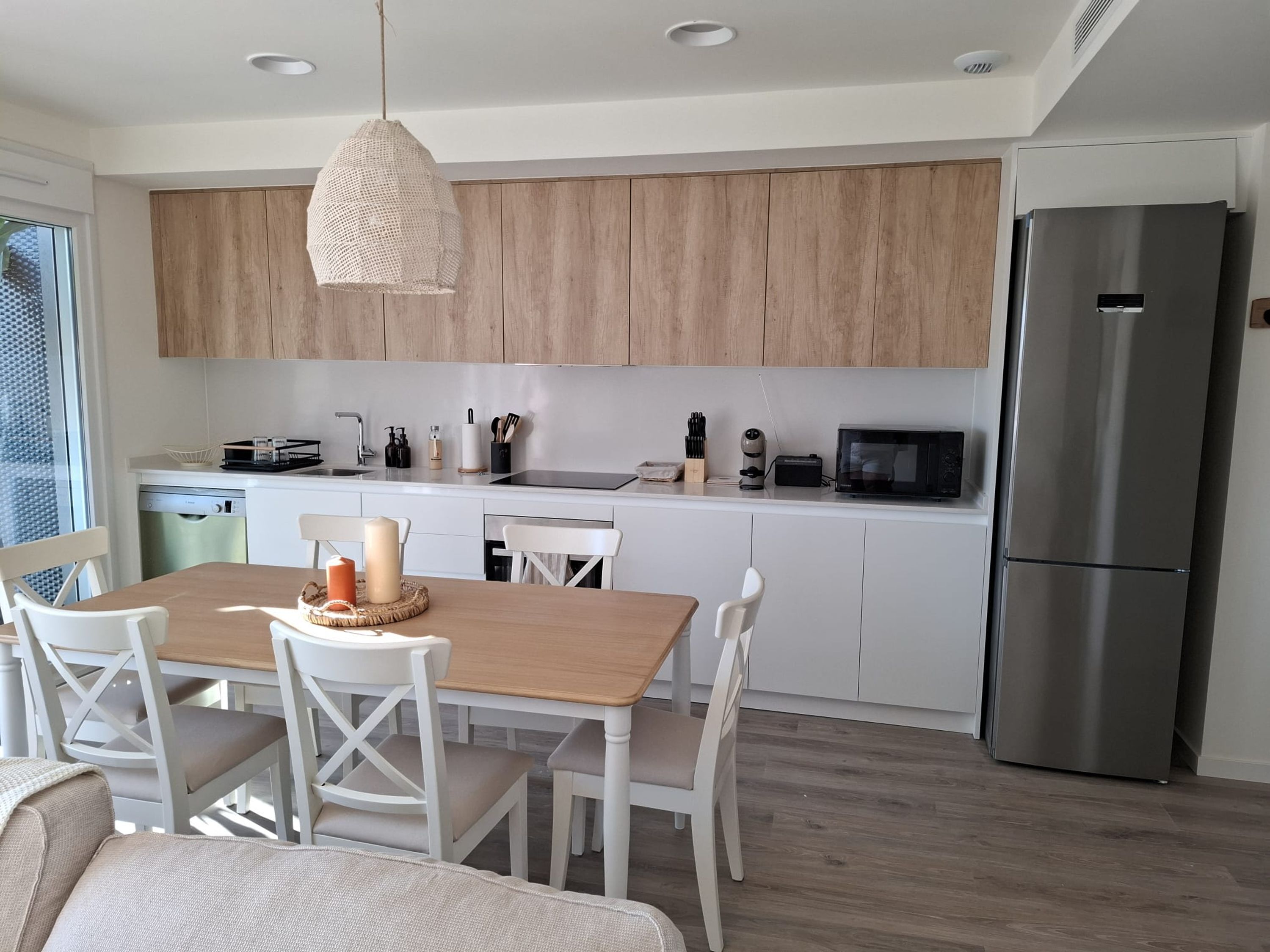 Una cocina moderna con armarios de madera, un refrigerador de acero inoxidable y un comedor con sillas blancas y una mesa de madera.