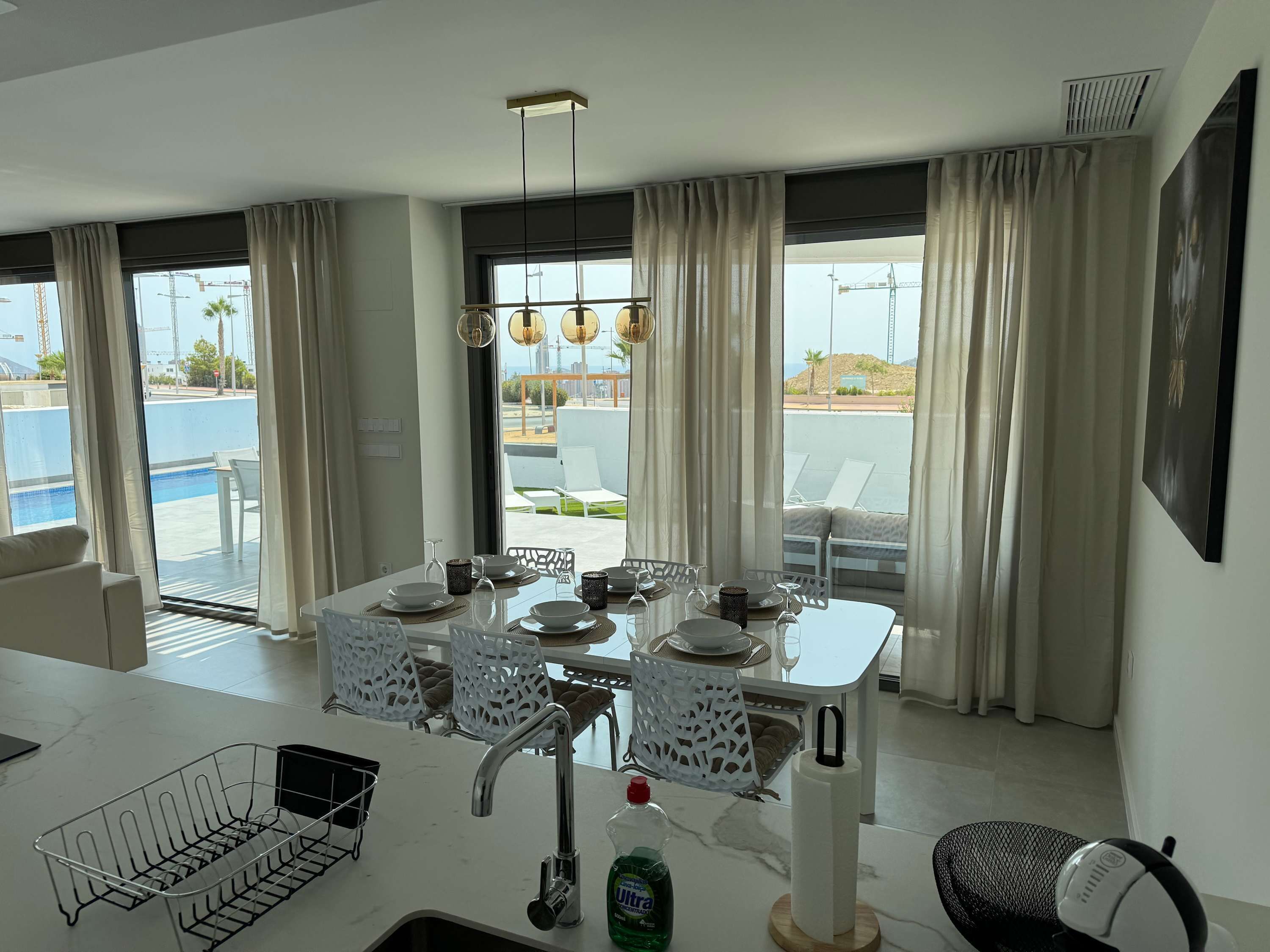 Una cocina moderna con comedor, ventanas amplias y vistas a la piscina y zona de estar exterior.