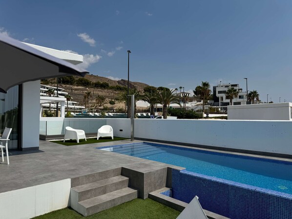 A modern outdoor pool area with a clear view of the surrounding landscape, including a hillside and buildings in the background. - Resort Seascape Villa 8 by Bookaparadise (Finestrat)