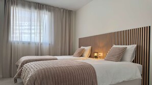 A modern bedroom with two beds, a wooden slat headboard, and a bedside table with a lamp. - Resort Seascape Villa 8 by Bookaparadise (Finestrat)