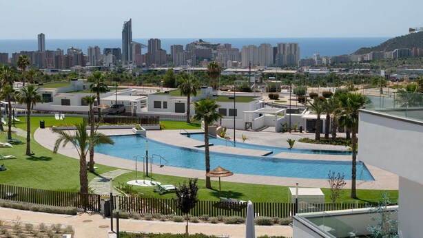 A resort with a swimming pool, palm trees, and a view of the city skyline. - Resort Seascape Villa 8 by Bookaparadise (Finestrat)
