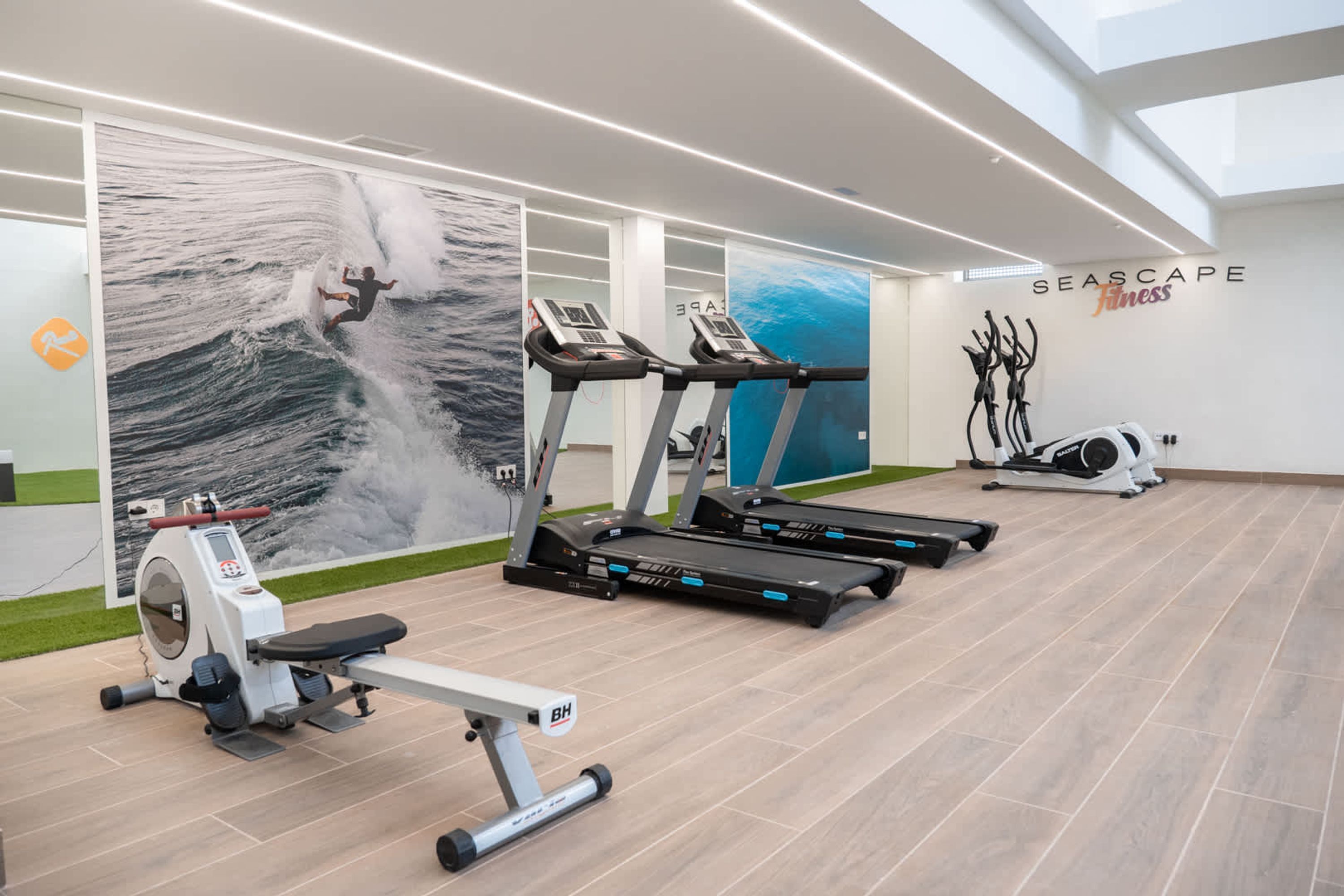 A modern gym with treadmills, a rowing machine, and a wall mural of a surfer.