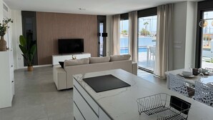 A modern living room with a flat-screen TV, a sofa, a marble coffee table, and a dining area with a pool view. - Resort Seascape Villa 8 by Bookaparadise (Finestrat)