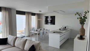 A modern living room with a sofa and a dining area with a white table and chairs. - Resort Seascape Villa 8 by Bookaparadise (Finestrat)