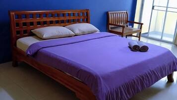 Una cama con cabecera de madera, colcha morada y dos almohadas. Hay una silla al lado de la cama.