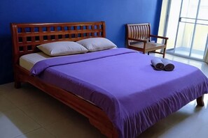 A bed with a wooden headboard, a purple bedspread, and two pillows. There is a chair next to the bed. - Peamsuk Sweet Prachin Buri (Prachinburi)