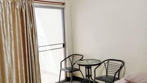 A room with a bed, two black metal chairs, a small round table, and a large window with curtains. - Peamsuk Sweet Prachin Buri (Prachinburi)