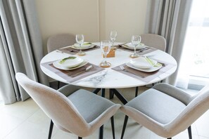 A round dining table with four chairs, set with plates, cutlery, and wine glasses. - Barsha Heights Sleeps 3 in an Amazing Location (Dubai)