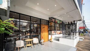 A modern cafe with a glass facade, outdoor seating, and a wooden door. - ZJ House(Phuket Town) (Phuket)