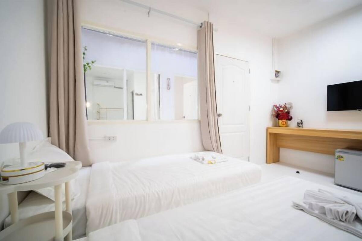 Habitación de hotel con dos camas, un escritorio con lámpara, un televisor montado en la pared y una mesita con un jarrón de flores.