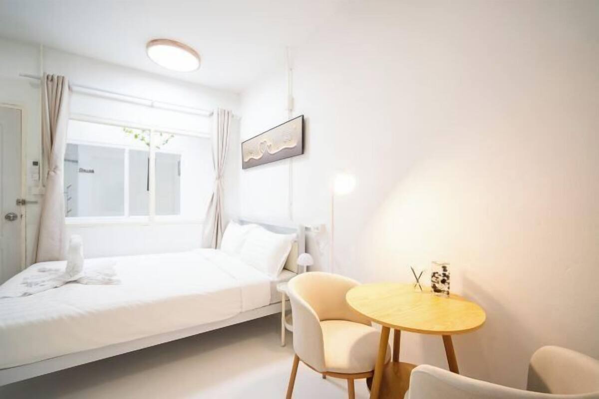 Habitación de hotel con cama, dos sillas, una mesita redonda, ventana con cortinas, un cuadro en la pared y una lámpara en el techo.
