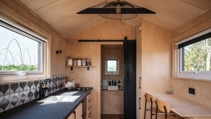 A compact kitchen with a black countertop, wooden cabinets, a built-in sink, and a window overlooking greenery. - Cosy Couple's Cabin w/Hot Tub (How Caple)