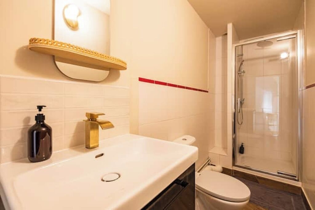 Un baño con lavamanos blanco, grifo dorado y cabina de ducha de vidrio.