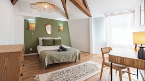 Ein Schlafzimmer mit einem Bett, einer Holzkommode, einem Esstisch mit Stühlen, einem gemusterten Teppich und einer Decke mit sichtbaren Balken.