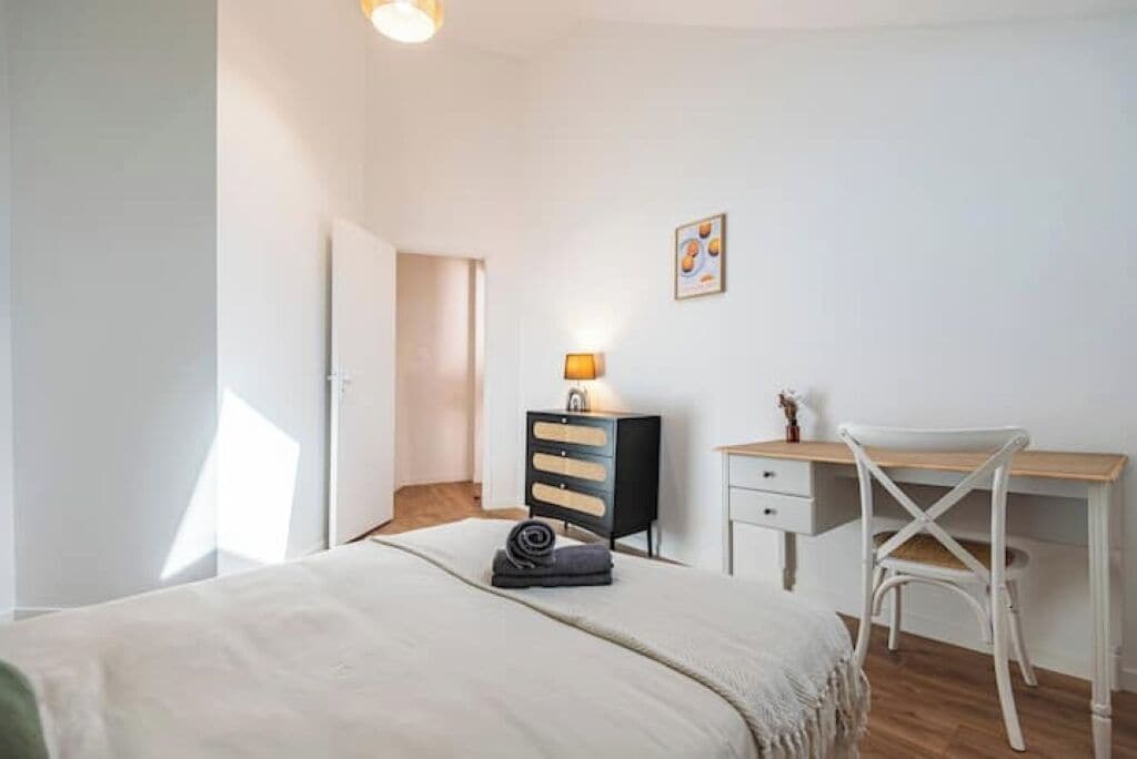 Un dormitorio con cama, escritorio, silla, cómoda y lámpara.