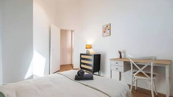 Un dormitorio con cama, escritorio, silla, cómoda y lámpara.