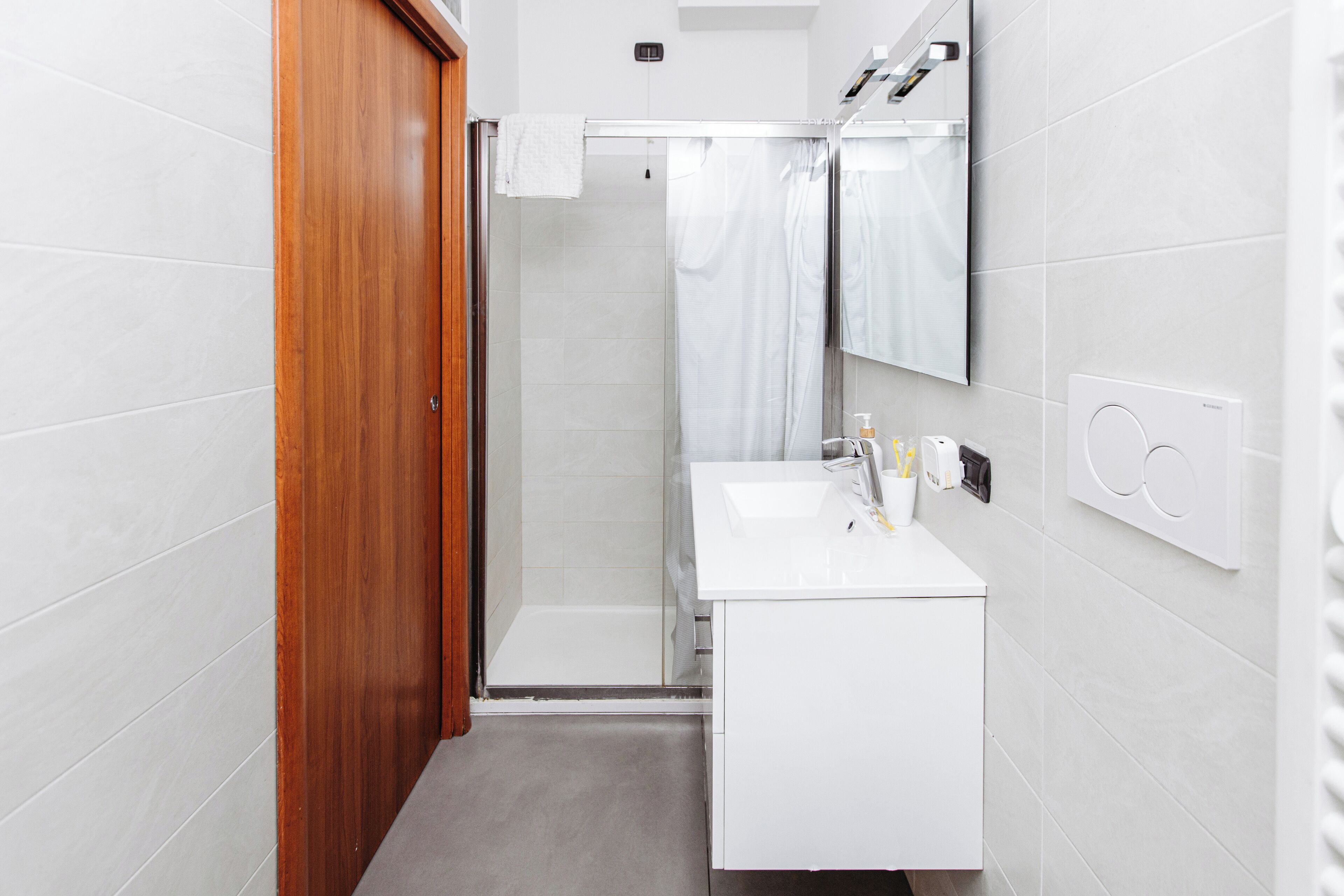 Ein modernes Badezimmer mit Holztür, Duschkabine aus Glas, Waschbecken in Weiß und einem Spiegel.