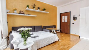 A modern bedroom with a bed, a small round table, and a coffee table. There are shelves with plants and decorative items on the wall.