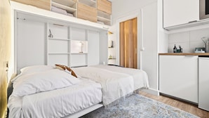 A bedroom with a bed, a built-in wardrobe, a kitchenette, and a door leading to another room. - Lovely Studio 10 mn walk to Louvre & Latin Quarter (Paris)