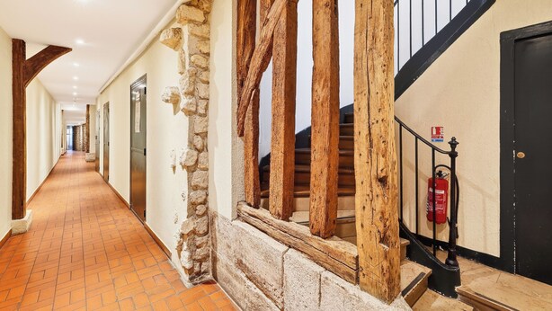 A corridor with stone walls, wooden beams, a tiled floor, and a staircase with a black railing. - Lovely Studio 10 mn walk to Louvre & Latin Quarter (Paris)
