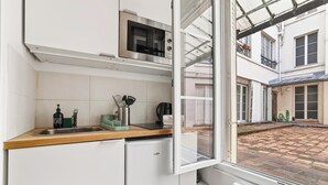 A kitchen with a microwave, sink, and utensils, and a view of a courtyard through a window. - Lovely Studio 10 mn walk to Louvre & Latin Quarter (Paris)