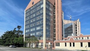 Een modern gebouw met een grote glazen gevel, een opvallende verticale structuur, en een kleiner, bijgebouwd pand met een gebogen dak.
