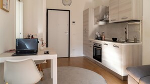 Een moderne keuken met een laptop op een bureau, een zithoek met een stoel en een bank.