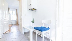 A white chair with a blue cushion in a bright hallway with white walls and a tiled floor. - Nice Room for Longstays @Margareten, Up to 2P (Vienna)