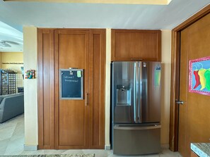 A kitchen with wooden cabinets, a stainless steel refrigerator, and a chalkboard with a welcome message. - Waves Relaxation Oceanfront 2BR Family Condo (Puerto Peñasco)