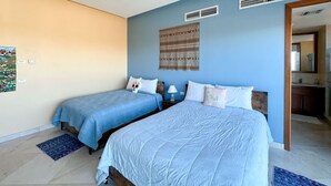 A bedroom with two beds, a ceiling fan, wall art, and a bathroom visible through an open door. - Waves Relaxation Oceanfront 2BR Family Condo (Puerto Peñasco)