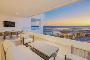 A modern balcony with a view of the ocean at sunset, furnished with white sofas and a table. - Beachfront Elegance at Las Palomas (Puerto Peñasco)