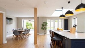 A modern kitchen with a central island, pendant lighting, and a dining area with a wooden table and chairs. - Modern 5-bedroom Retreat Nr Coast (Emsworth)